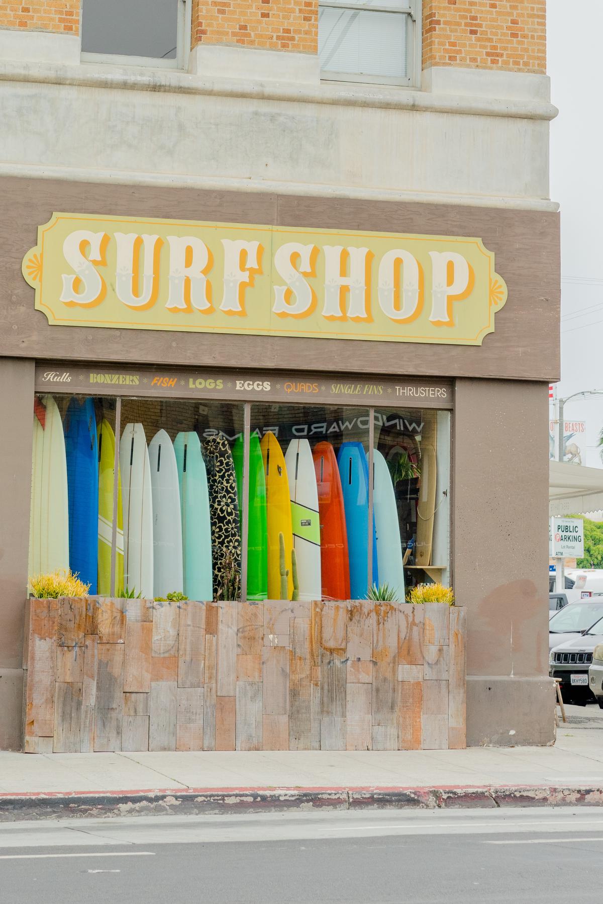 A photo of a modern surf shop building with a banner that reads PB Surf Shop in front, with bikes parked outside. This shop is located in a beach town and has a relaxed atmosphere.