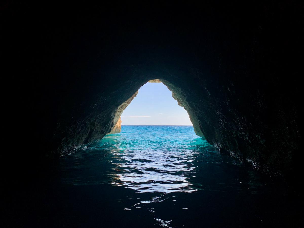 A person kayaking through a sea cave with sunlight shining in from above.