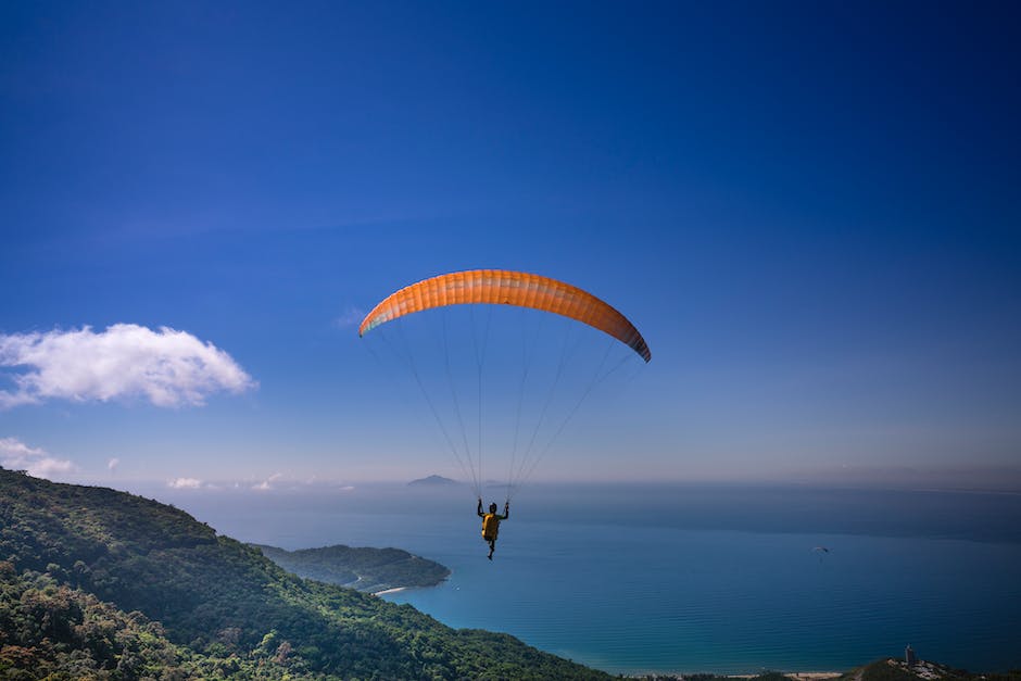 A person paragliding over the ocean with Torrey Pines cliffs in the background.