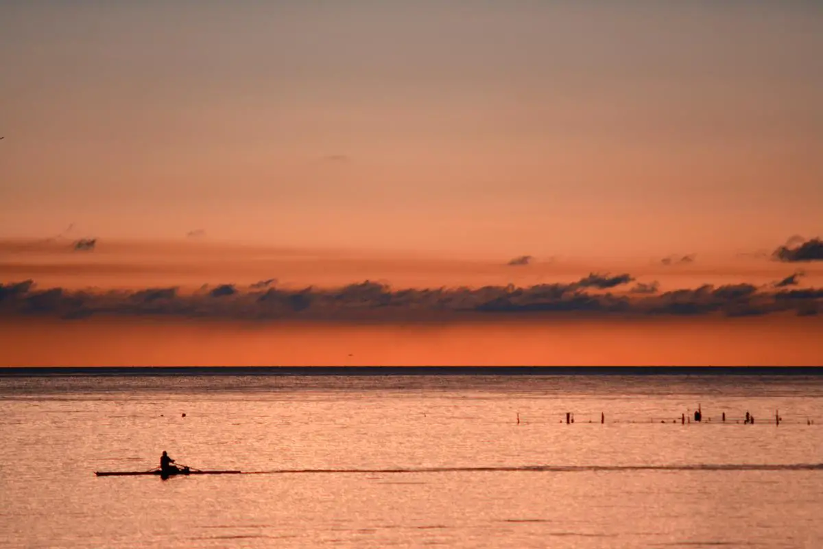 A photo of kayakers paddling along a serene coastline during sunset, with the silhouette of rugged cliffs in the distance.
